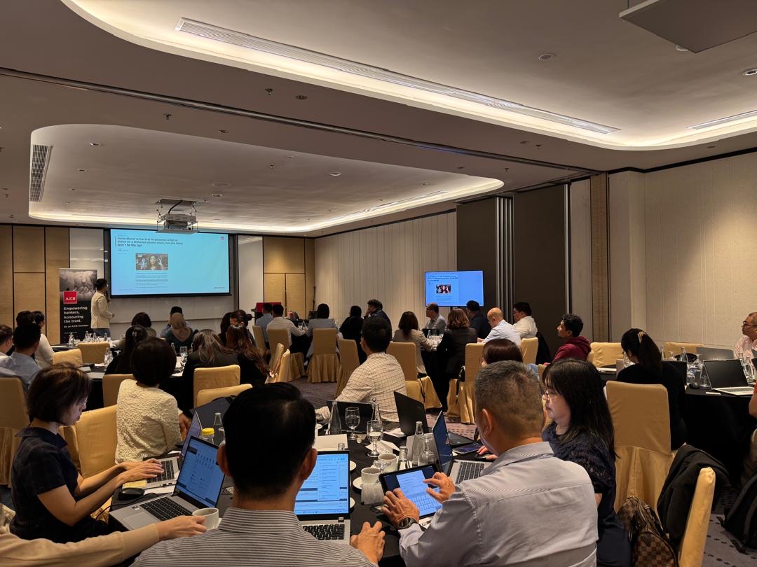 A Nexor AI trainer presenting to a room of participants working on laptops, with a Microsoft 365 Copilot screen projected behind