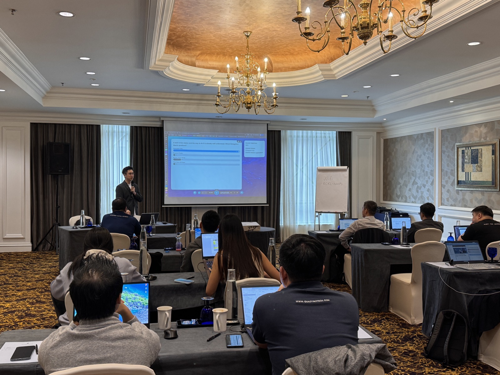 A Nexor AI trainer presenting a live quiz on screen to participants seated at laptops